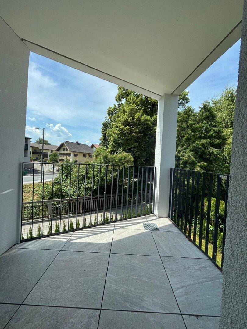 Heller Balkon mit modernen Fliesen und schwarzem Geländer, bietet einen grünen Ausblick und viel Tageslicht.