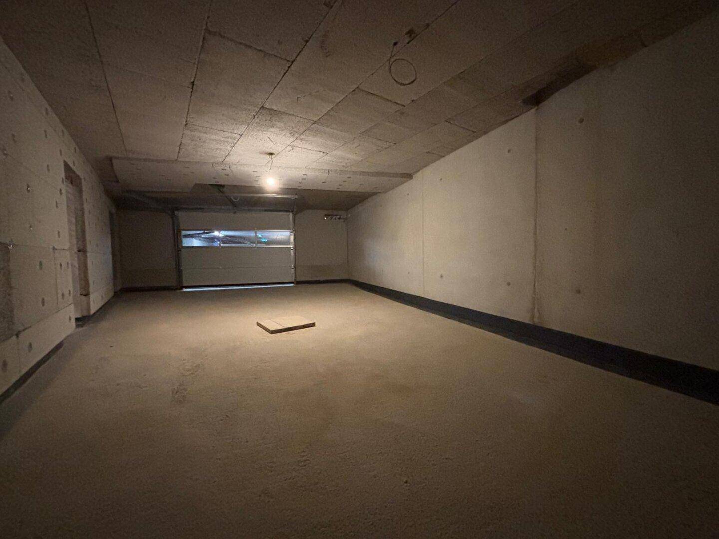 Dunkler, unfertiger Garagenbereich mit Rolltor, bietet viel Stauraum und Parkmöglichkeiten im Untergeschoss.