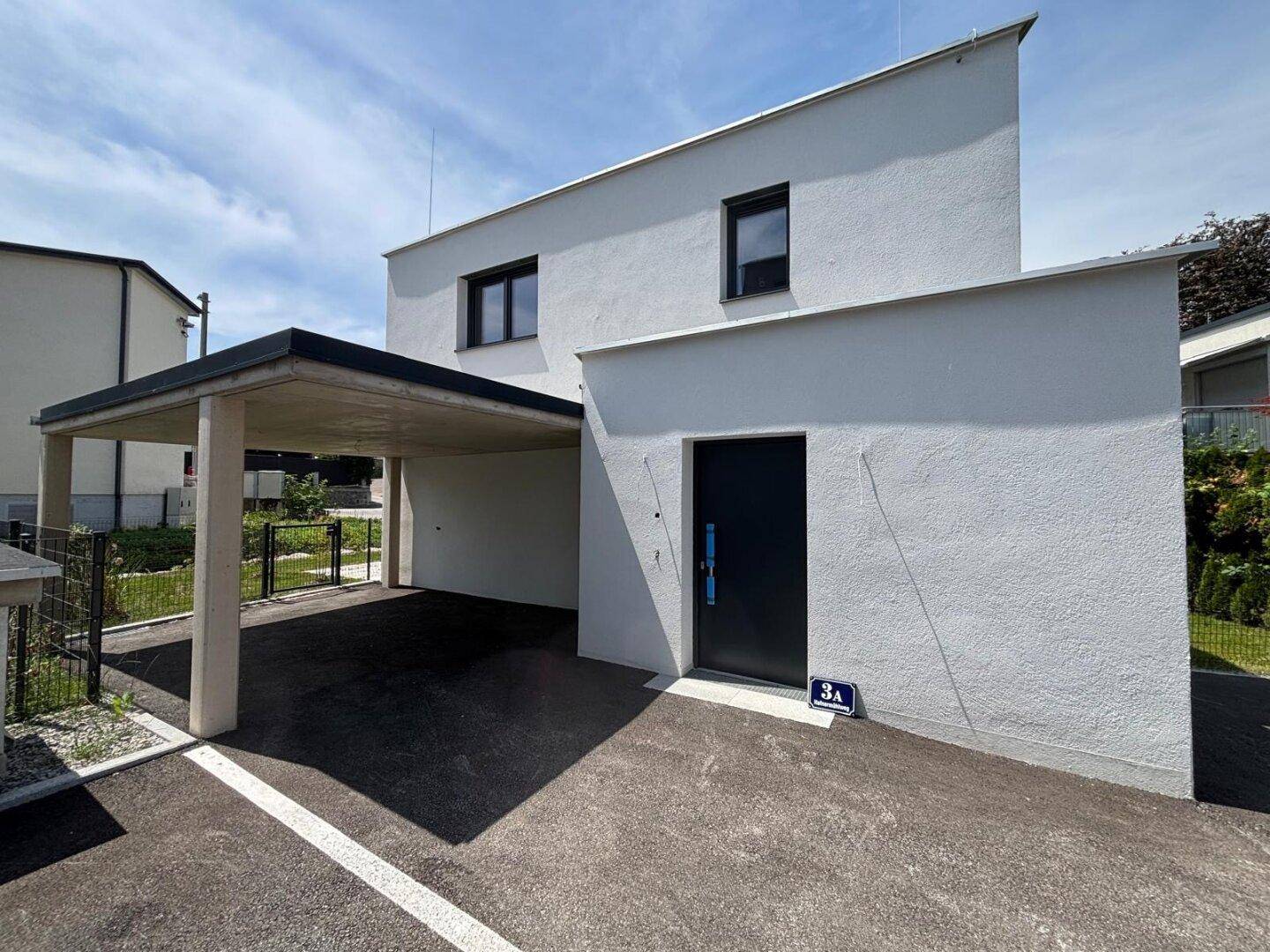 Eingangsbereich des modernen Hauses mit schwarzer Tür und angrenzendem Carport, in gehobener Bauweise.
