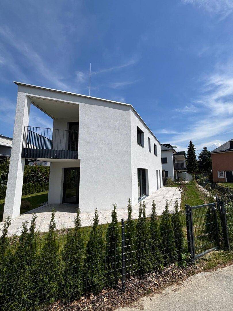 Seitenansicht des modernen Gebäudes mit Balkon und gepflegter Hecke im Vordergrund, in hochwertiger Ausführung.