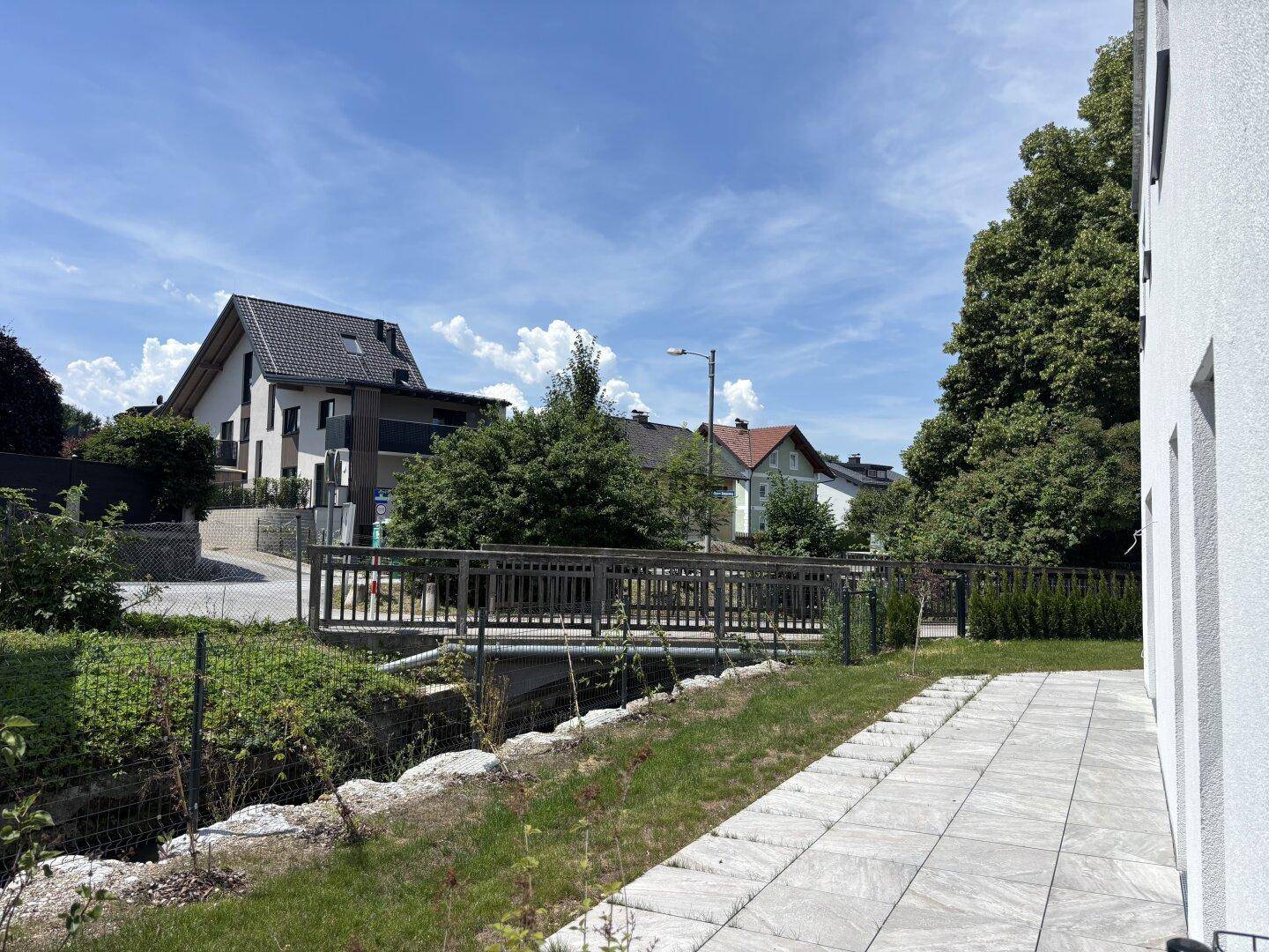 Gepflasterter Terrassenbereich am Bachlauf mit Blick auf die umliegenden Häuser und viel natürlichem Licht.