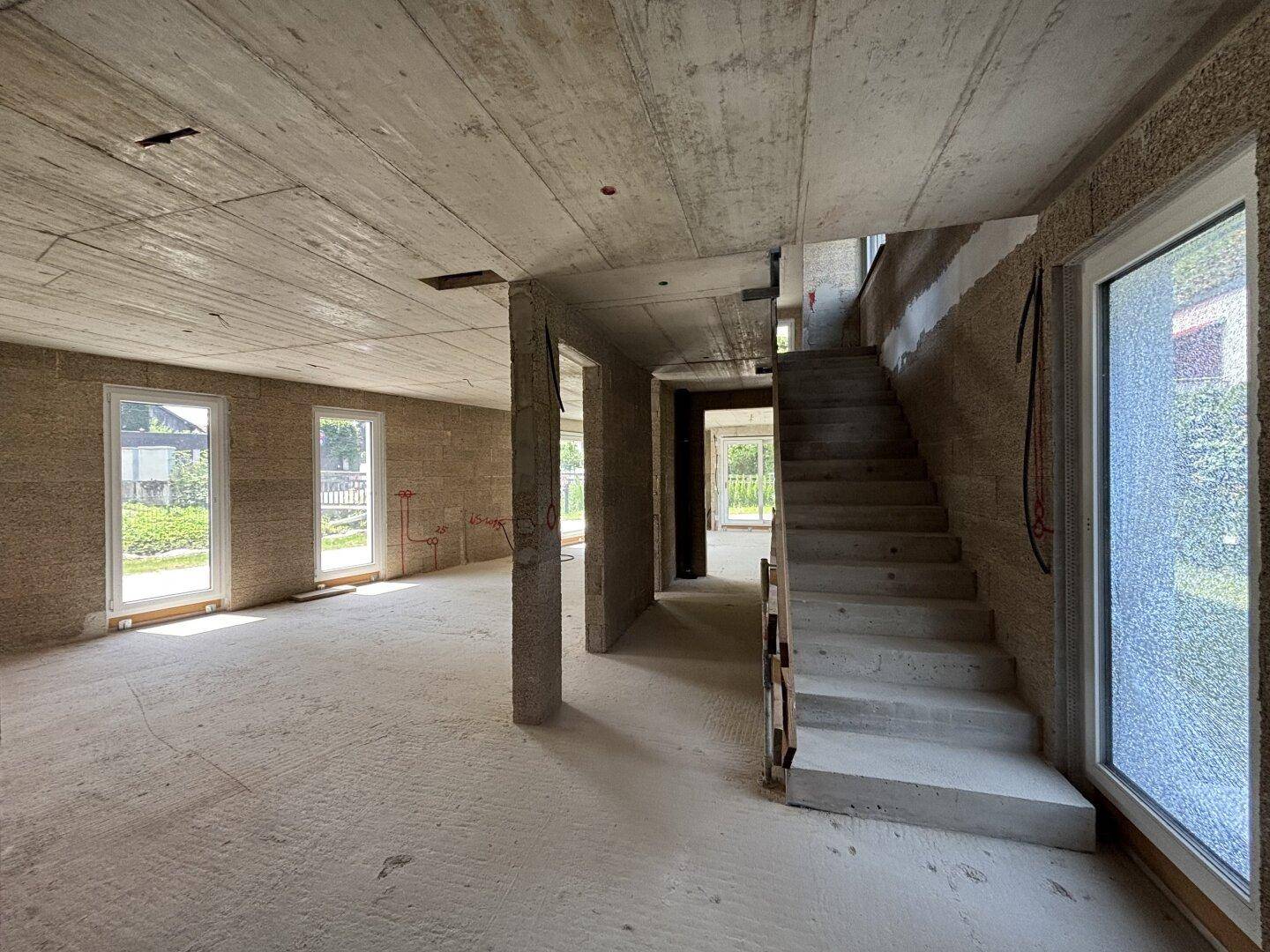 Rohbau eines Innenraums mit Betondecken, Wänden und einer massiven Betontreppe, bietet viel Tageslicht.