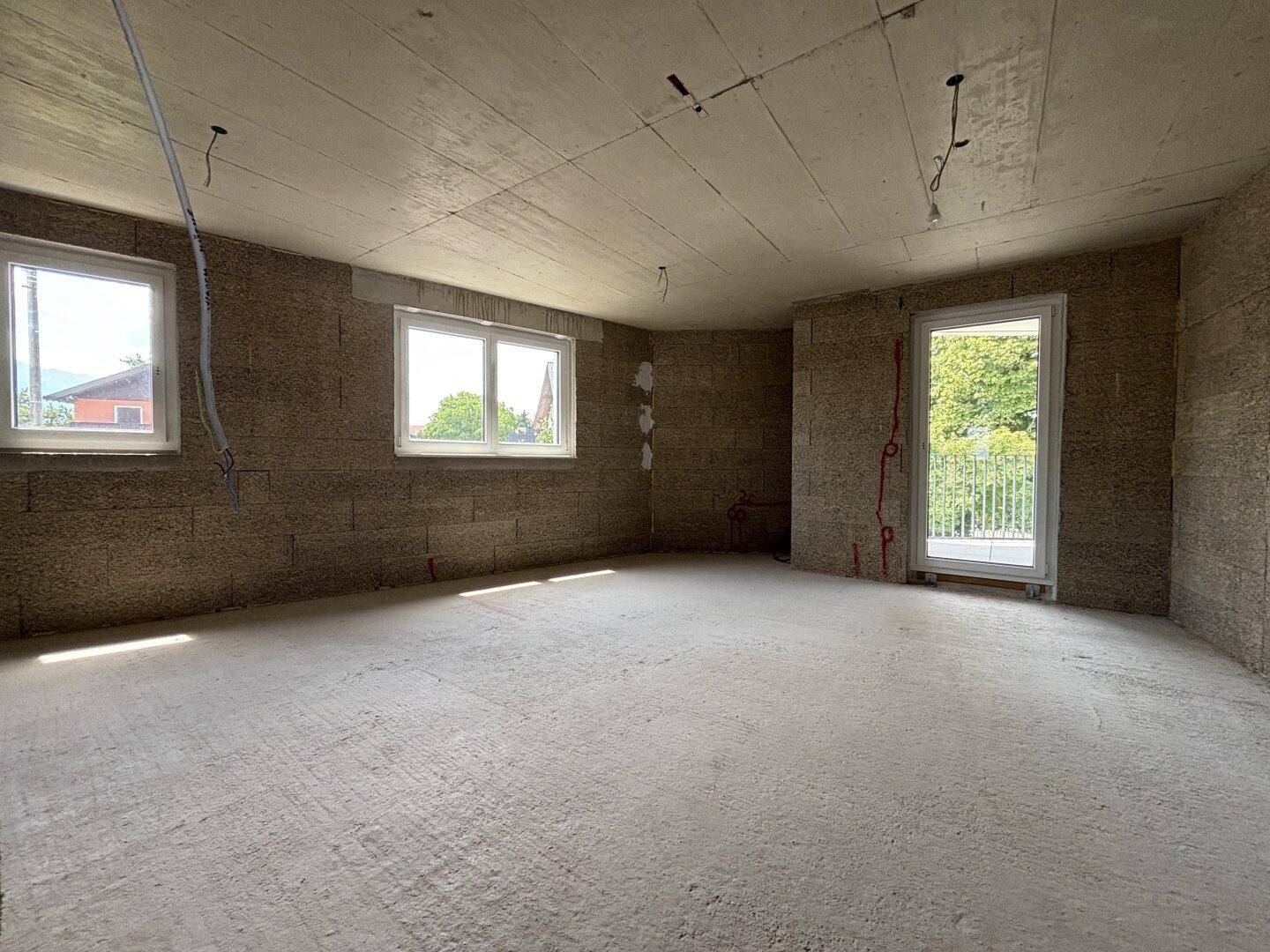 Rohbau eines Zimmers mit Fenstern und Zugang zu einem kleinen Balkon, bietet viel Tageslicht und Potenzial.