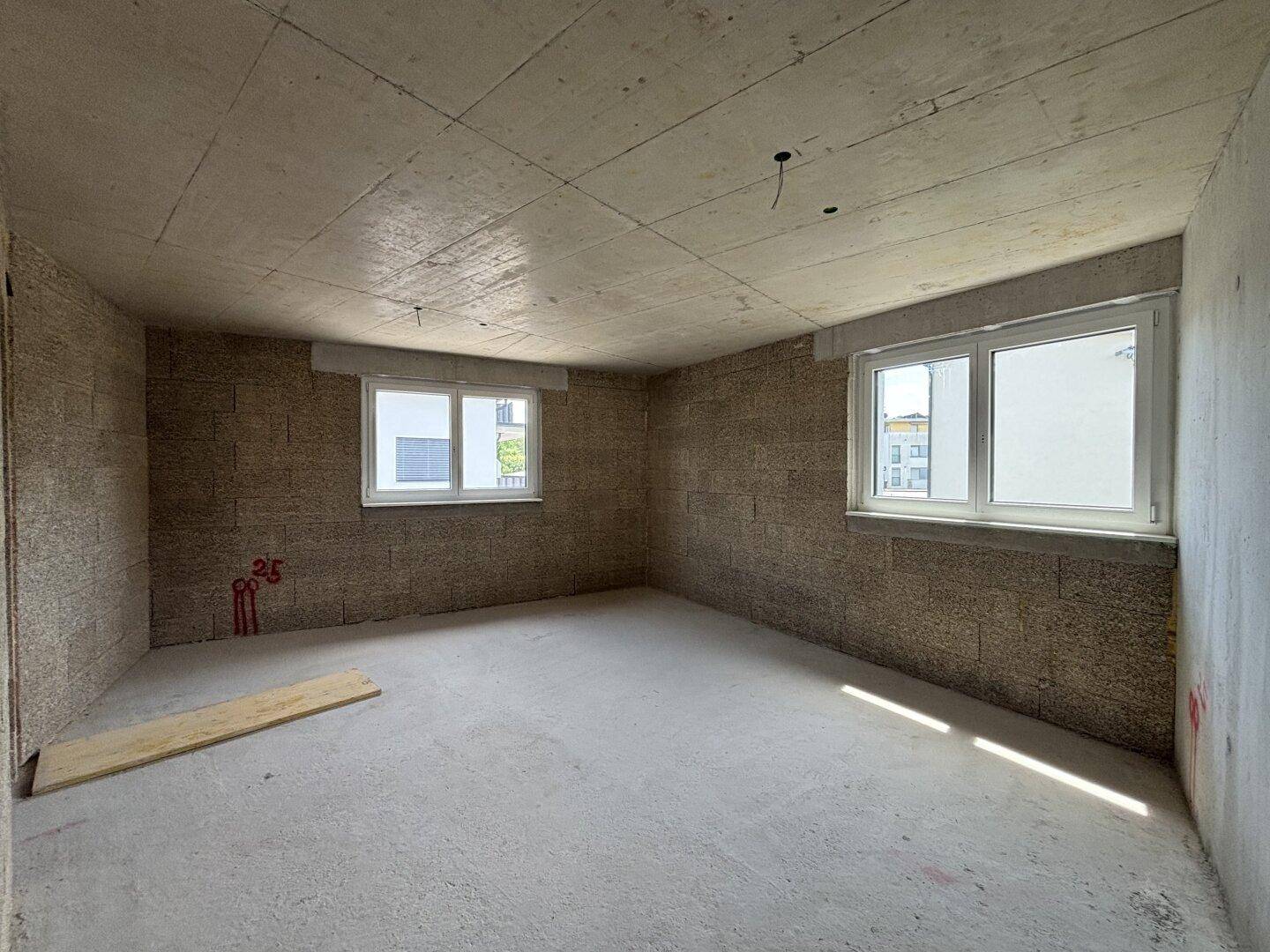 Rohbau eines hellen Zimmers mit zwei Fenstern, ideal für ein Schlafzimmer oder Büro, mit viel natürlichem Licht.