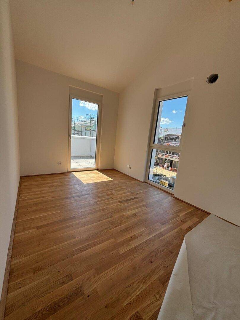 Lichtdurchfluteter Raum mit Holzboden, großen Fenstern und direktem Zugang zum Außenbereich.