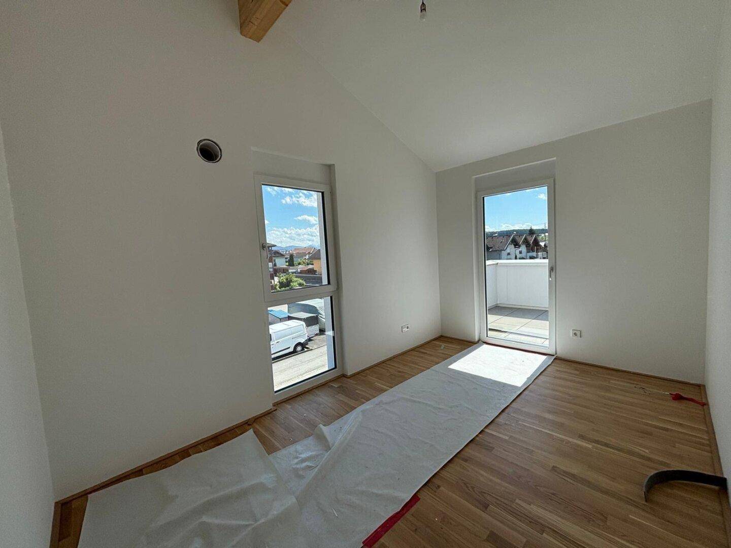 Helles Zimmer mit Holzboden, schrägen Wänden und Zugang zu einer Terrasse durch eine Fenstertür.