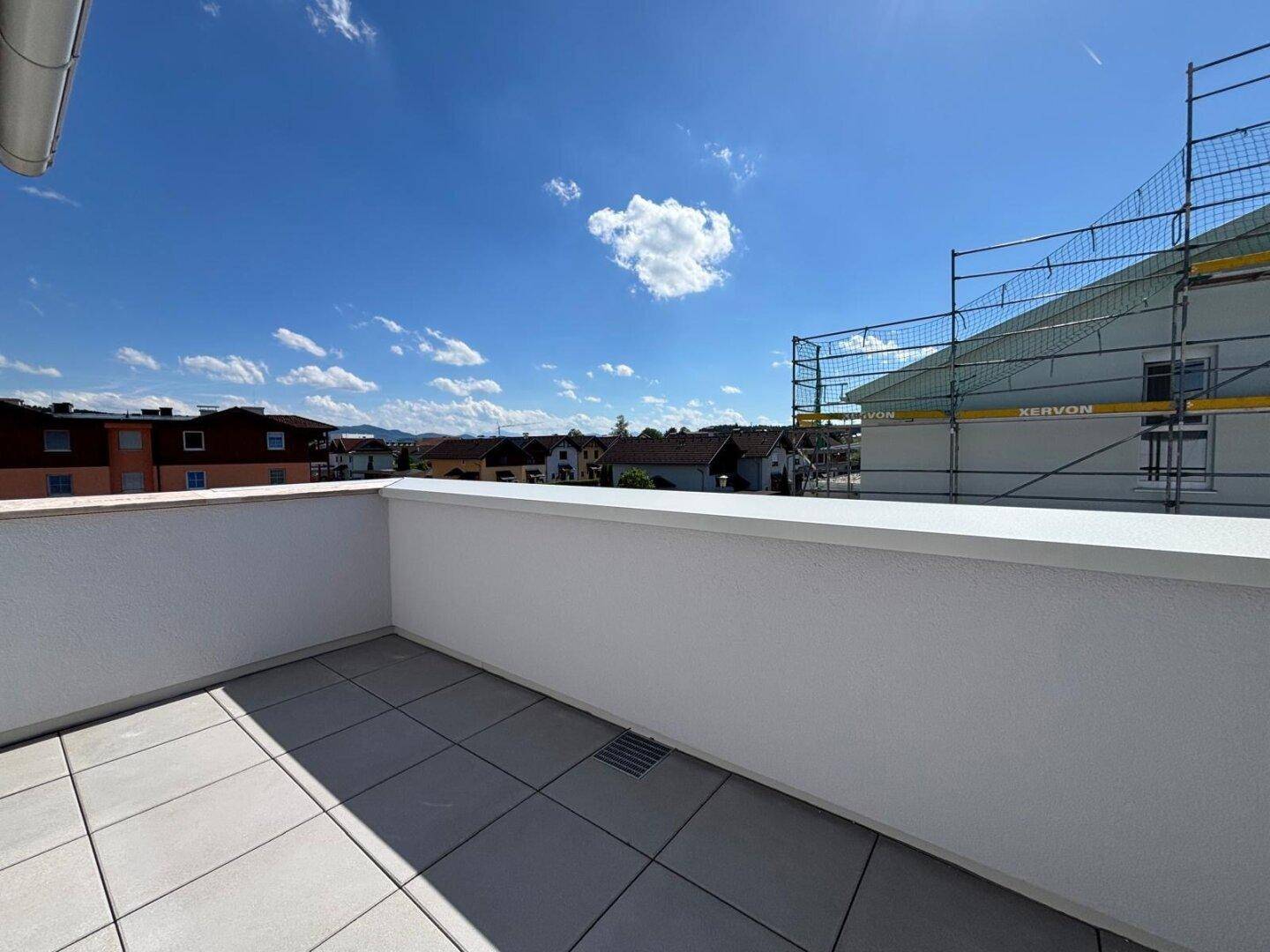 Sonniger Terrassenbereich mit grauen Fliesen und Blick auf die umliegende Wohngegend und eine Baustelle.
