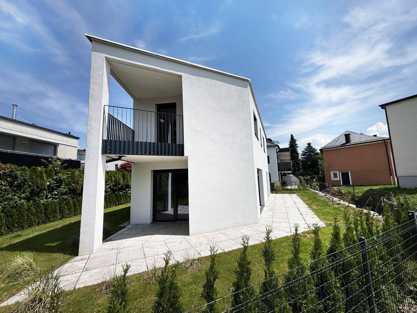 Moderne weiße Architektur mit klaren Linien, einem kleinen Balkon und gepflegtem Rasenbereich.