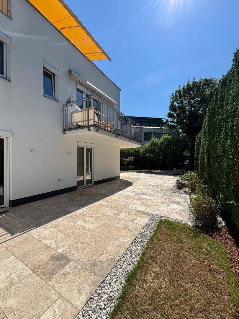 Moderne Hausfassade mit großer Terrasse, Balkon und Markise unter blauem Himmel.