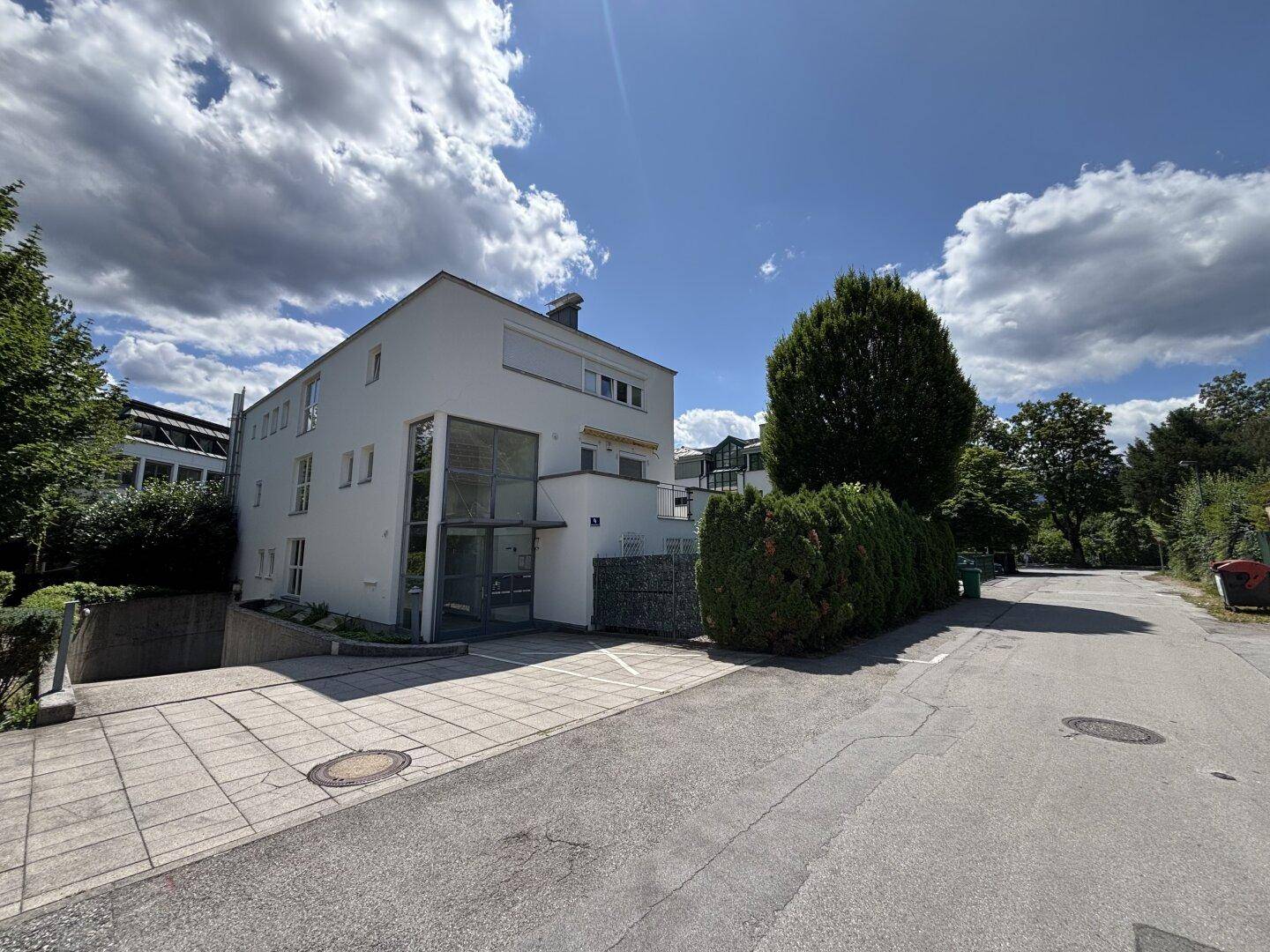 Ansicht des modernen Gebäudes von der Straße aus, umgeben von viel Grün und Bäumen.