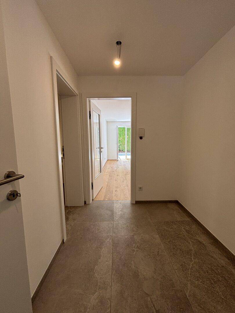 Heller Flur mit Fliesenboden, der zu einem weiteren Raum mit Holzboden führt.