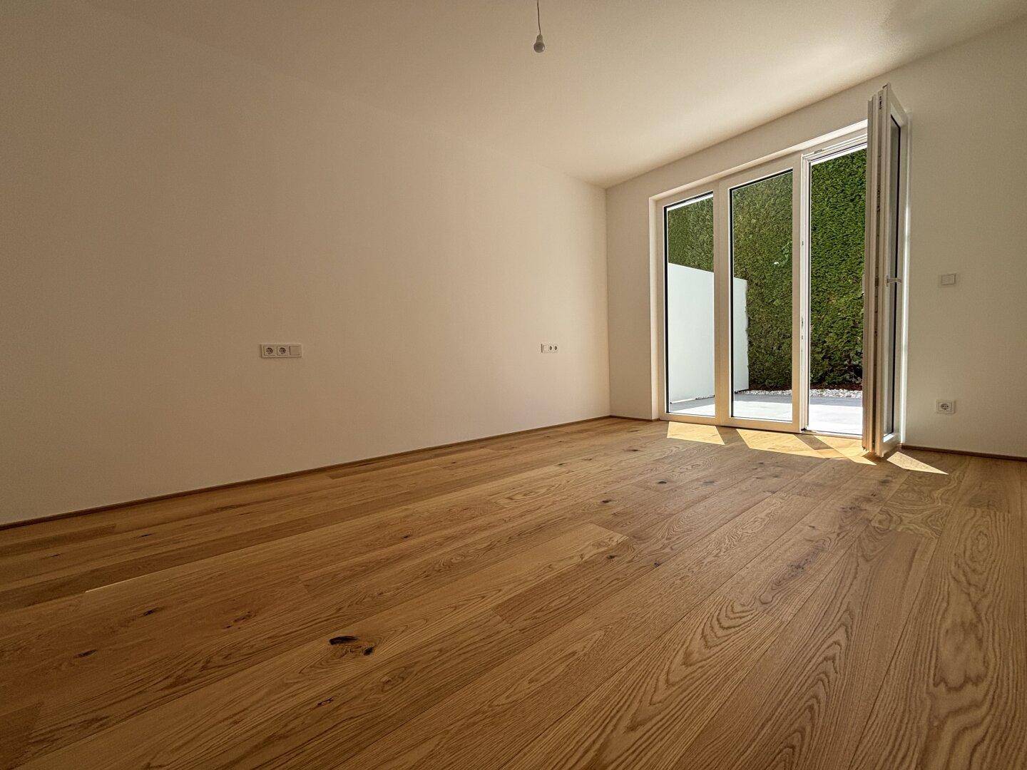 Heller Wohnraum mit hochwertigem Holzboden und viel Tageslicht durch die großen Terrassentüren.