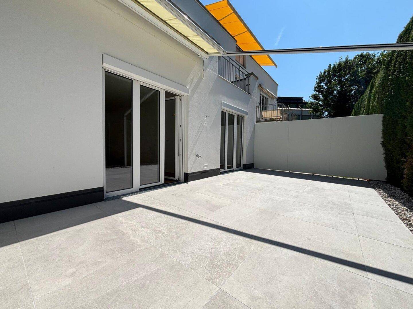 Geräumige, sonnige Terrasse mit Fliesenboden und ausfahrbarer Markise für angenehmen Schatten.