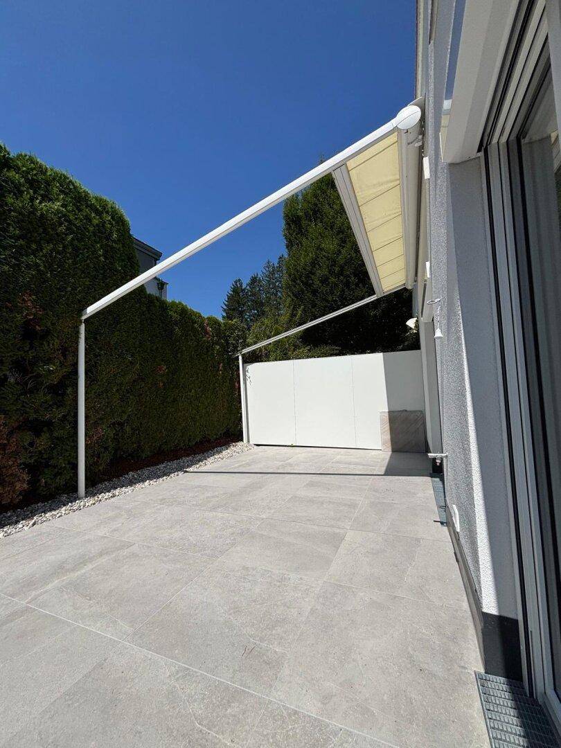 Große Terrasse mit moderner Markise und umgebender Hecke, ideal für entspannte Stunden im Freien.