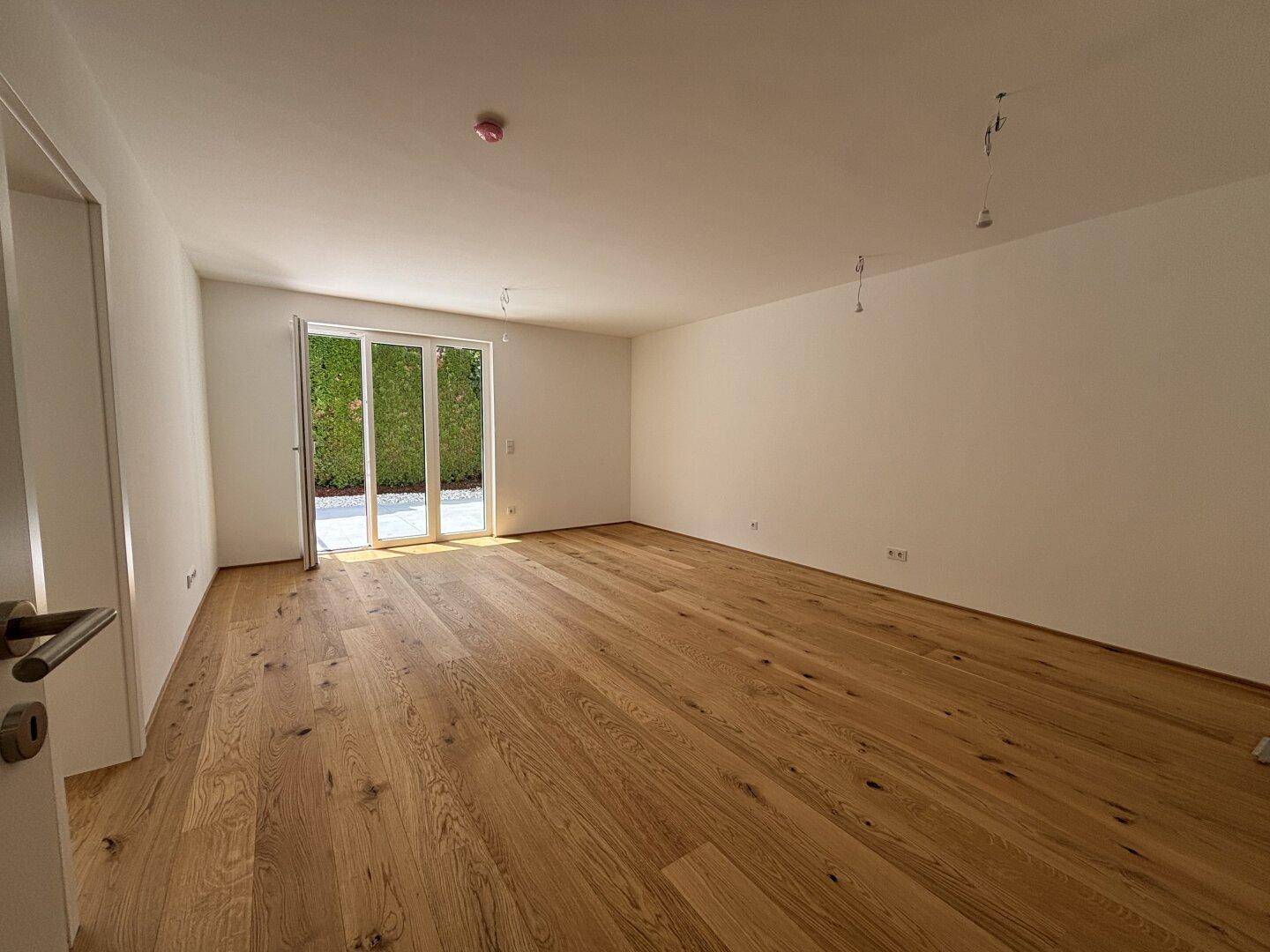 Geräumiger, heller Raum mit Eichenparkett und Zugang zu einem sonnigen Außenbereich durch große Fenster.