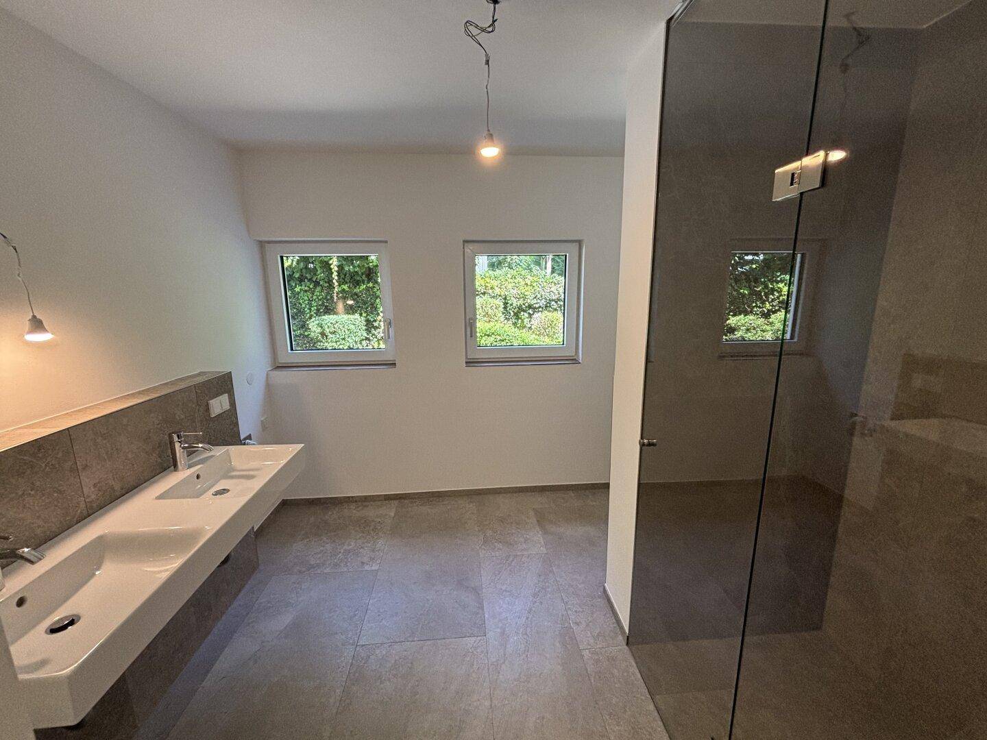 Helles Badezimmer mit zwei Fenstern, Doppelwaschbecken und moderner begehbarer Dusche.
