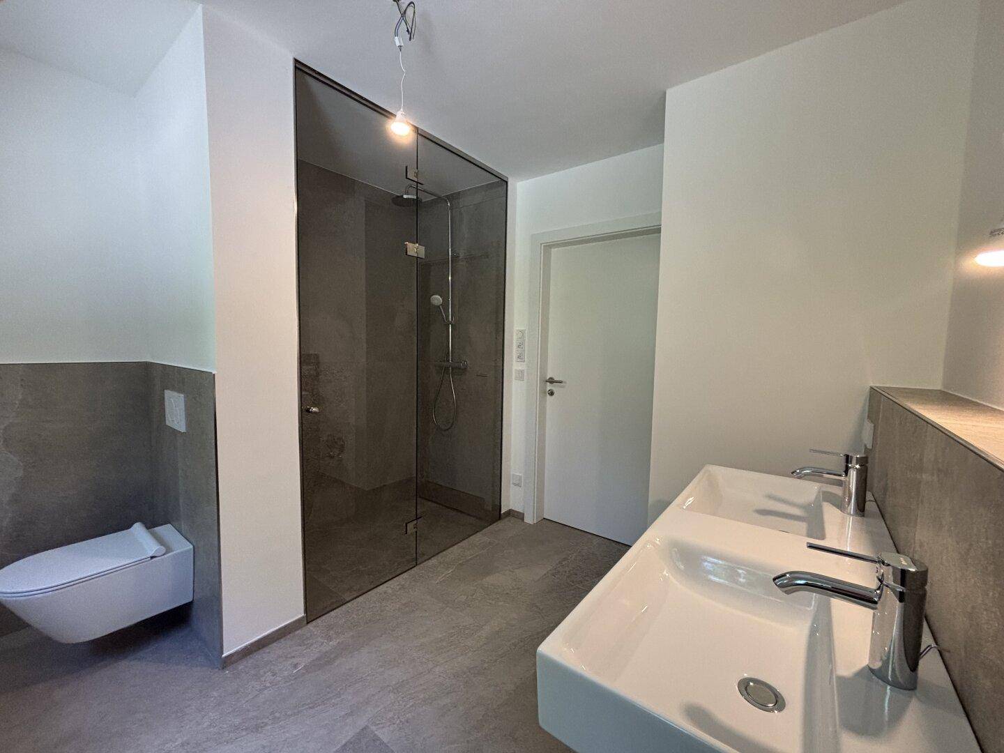 Modernes Badezimmer mit Doppelwaschbecken, großer Glasdusche und grauen Fliesen.