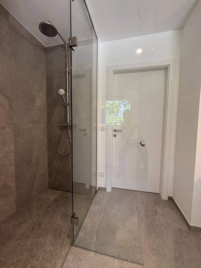 Großzügige, moderne begehbare Dusche mit Regenduschkopf und Glasabtrennung im Badezimmer.