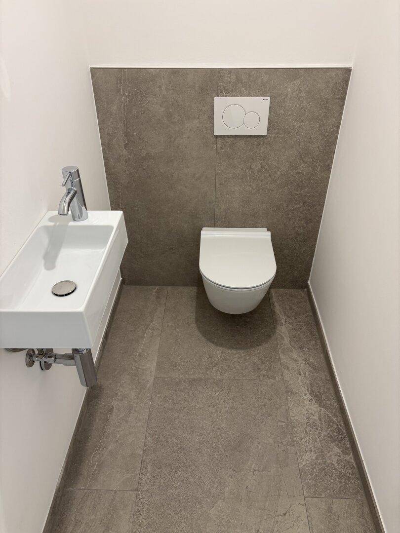 Kompaktes Gäste-WC mit wandhängender Toilette und kleinem Waschbecken in modernem Design.