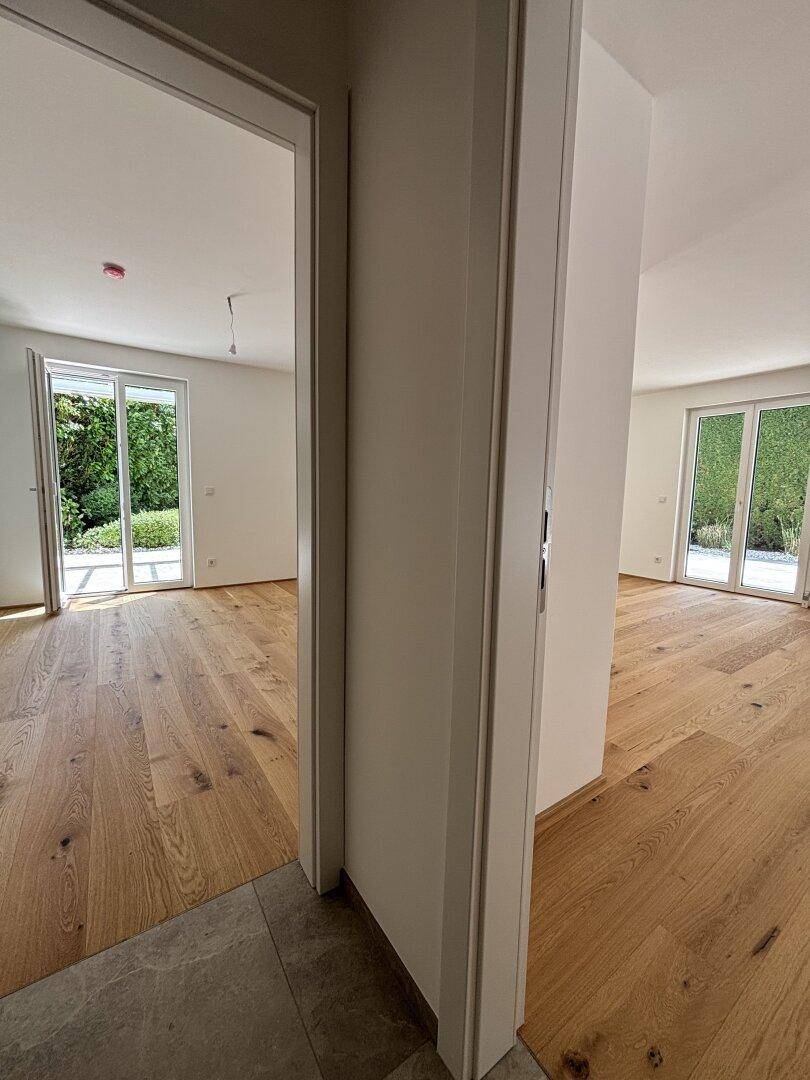 Blick vom Flur in den offenen Wohnbereich mit Eichenparkett und viel Tageslicht.