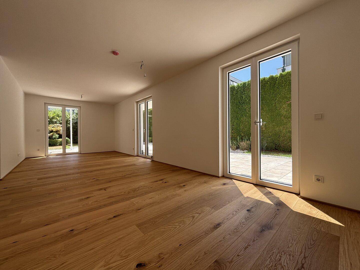 Heller, leerer Raum mit Eichenparkettboden und großen Fenstertüren zum Garten.