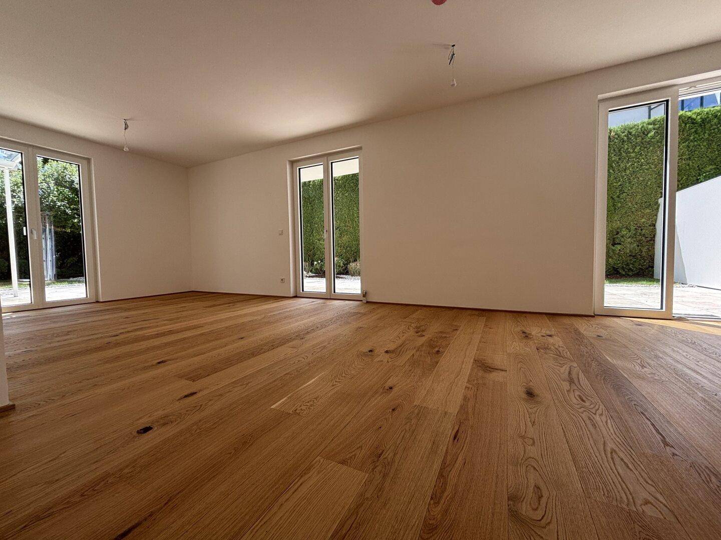 Geräumiger, unmöblierter Raum mit hellem Eichenparkett und Zugang zu mehreren Terrassenbereichen.
