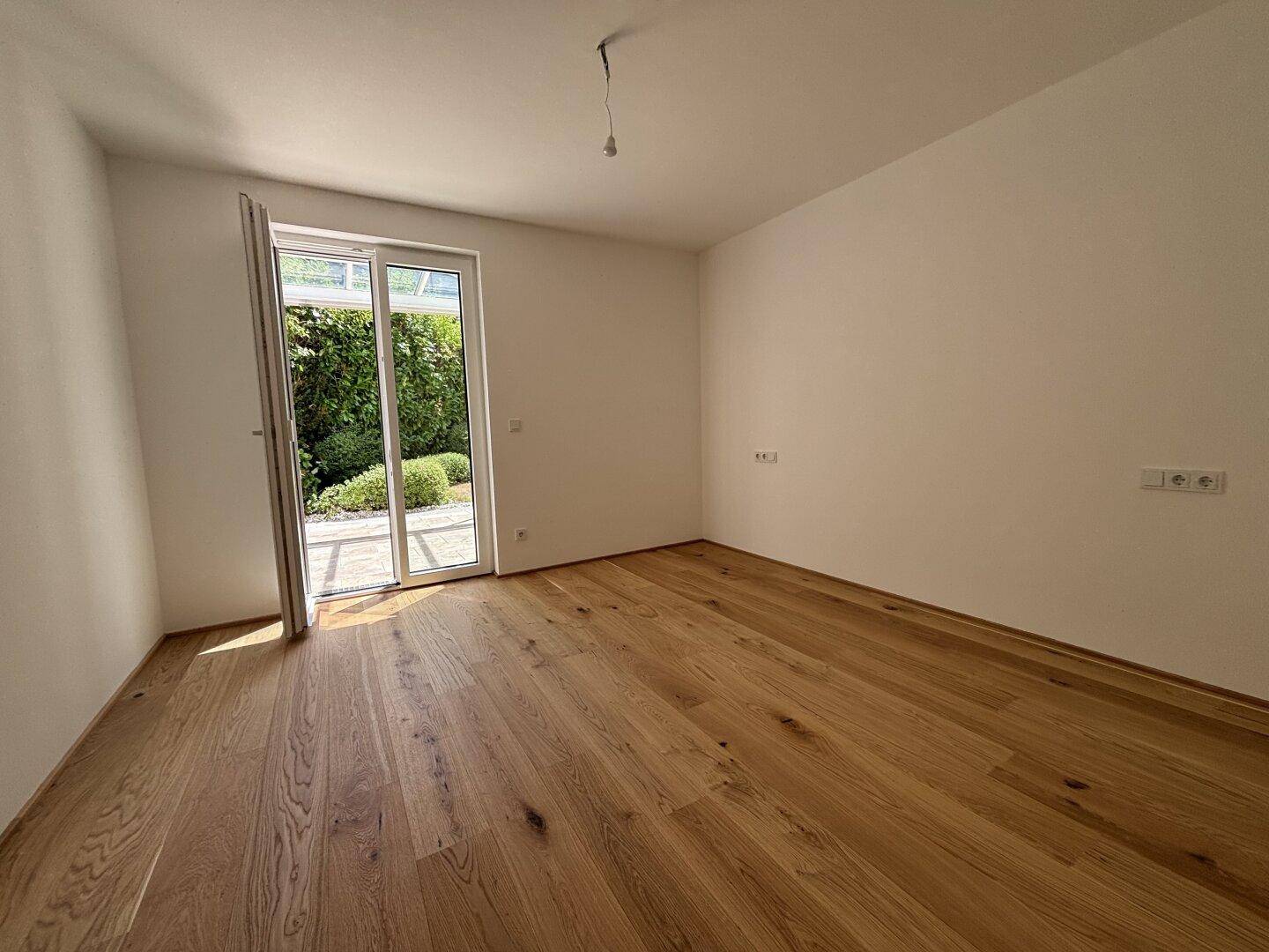 Helles Schlafzimmer mit Eichenparkettboden und Zugang zu einem privaten Außenbereich.