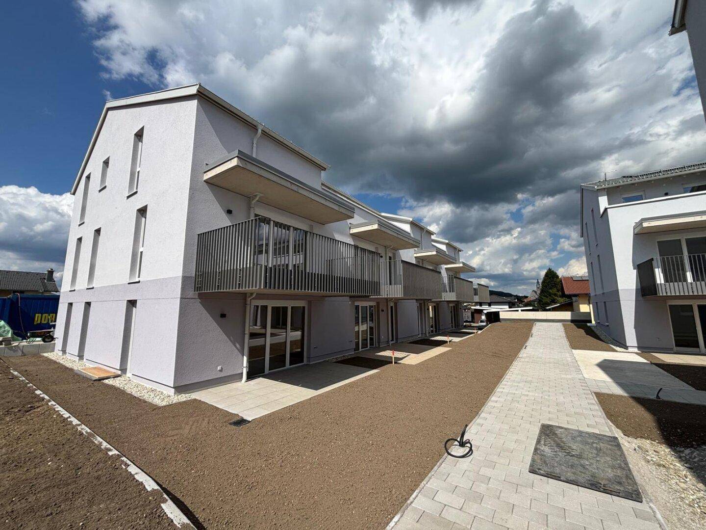 Neubau-Wohngebäude mit Balkonen und ebenerdigen Terrassen, umgeben von neu angelegten Wegen.