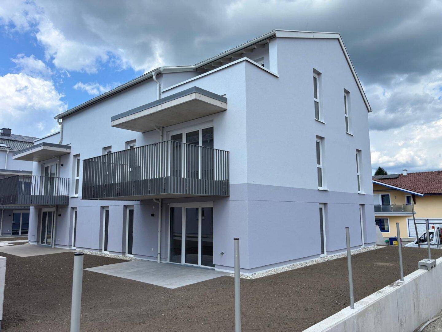 Eckansicht eines neuen Wohngebäudes mit modernen Balkonen und Terrassen im Erdgeschoss.