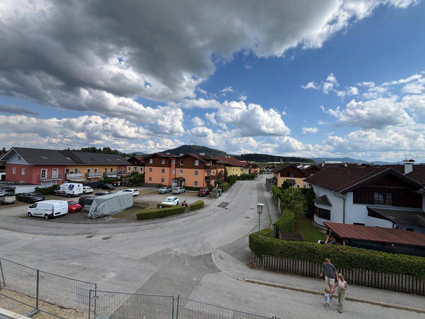 Weitläufige Ansicht einer Wohnsiedlung mit Häusern, Straße und Bergen im Hintergrund unter blauem Himmel.
