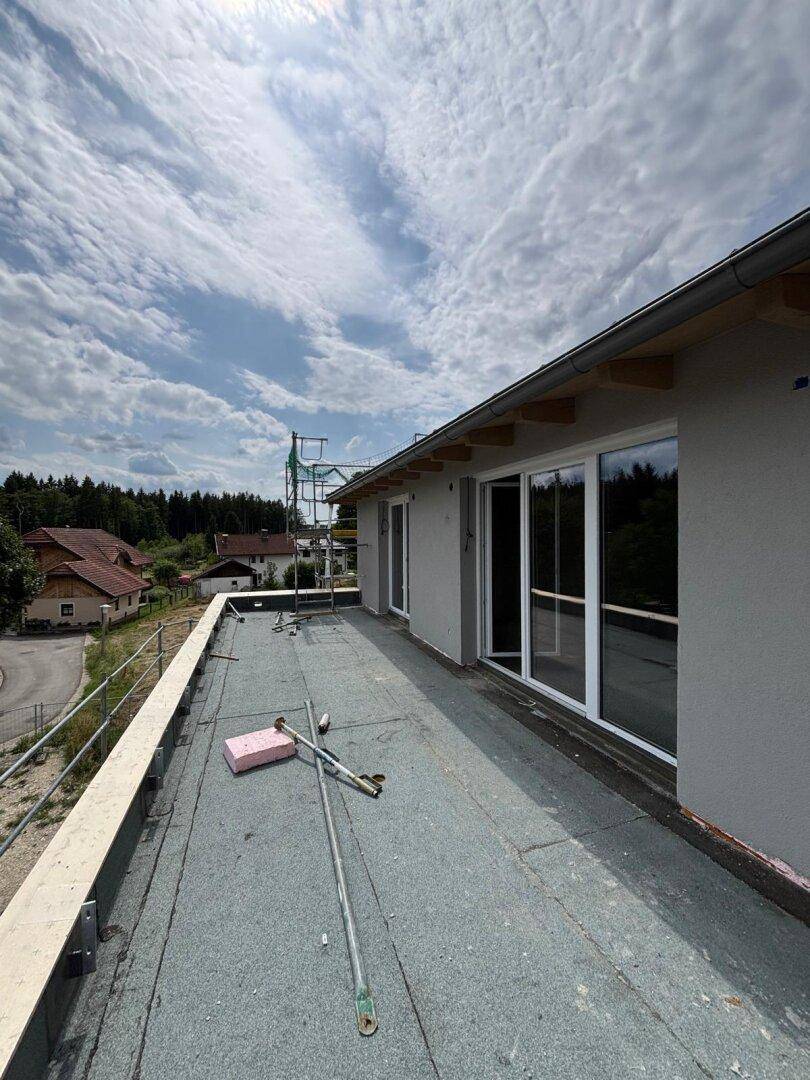 Unfertige Dachterrasse mit weitem Blick über die ländliche Umgebung und bewaldete Flächen.