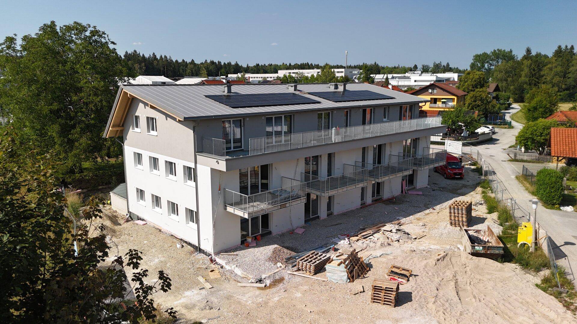 Neubau eines Mehrfamilienhauses im Bauzustand mit installierten Solarpaneelen auf dem Dach.