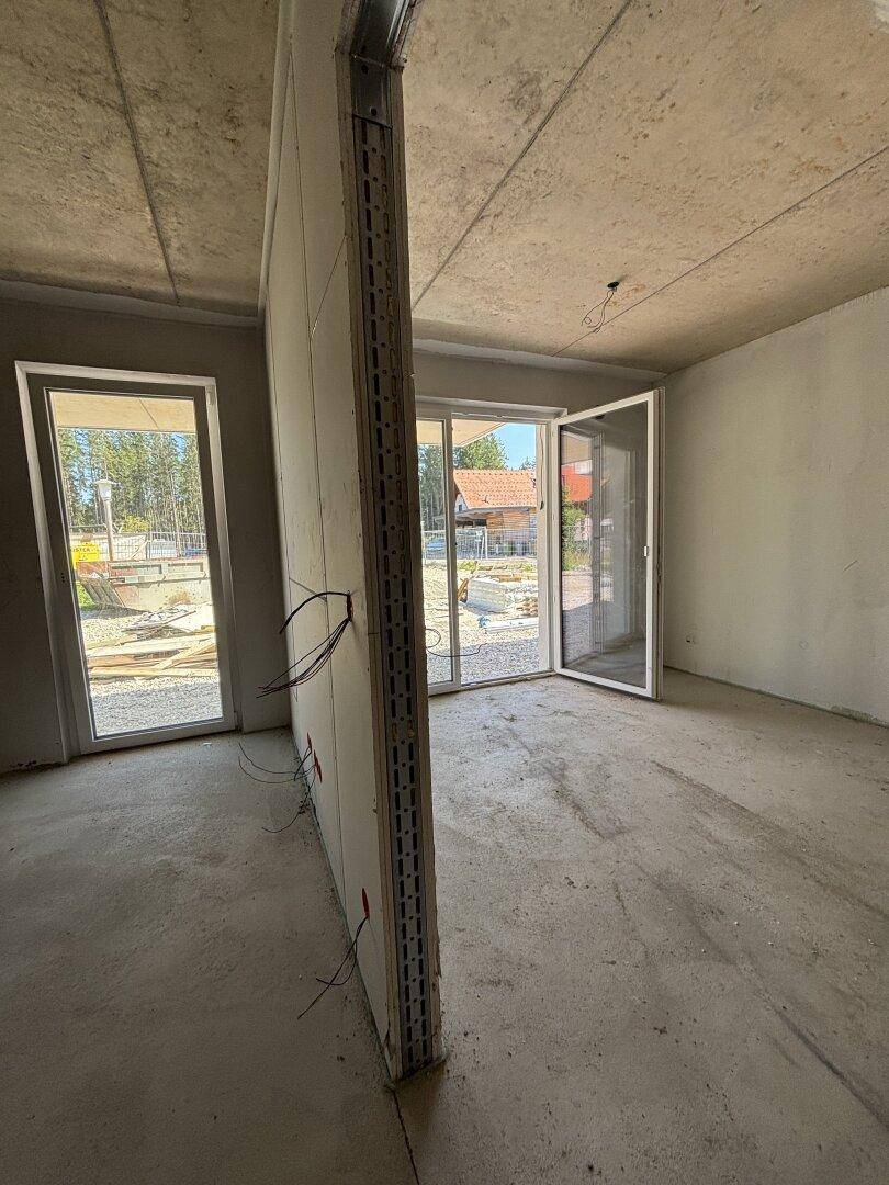 Rohbau eines Zimmers mit Betonboden, unverputzten Wänden und großen Fenstern zur Außenseite.
