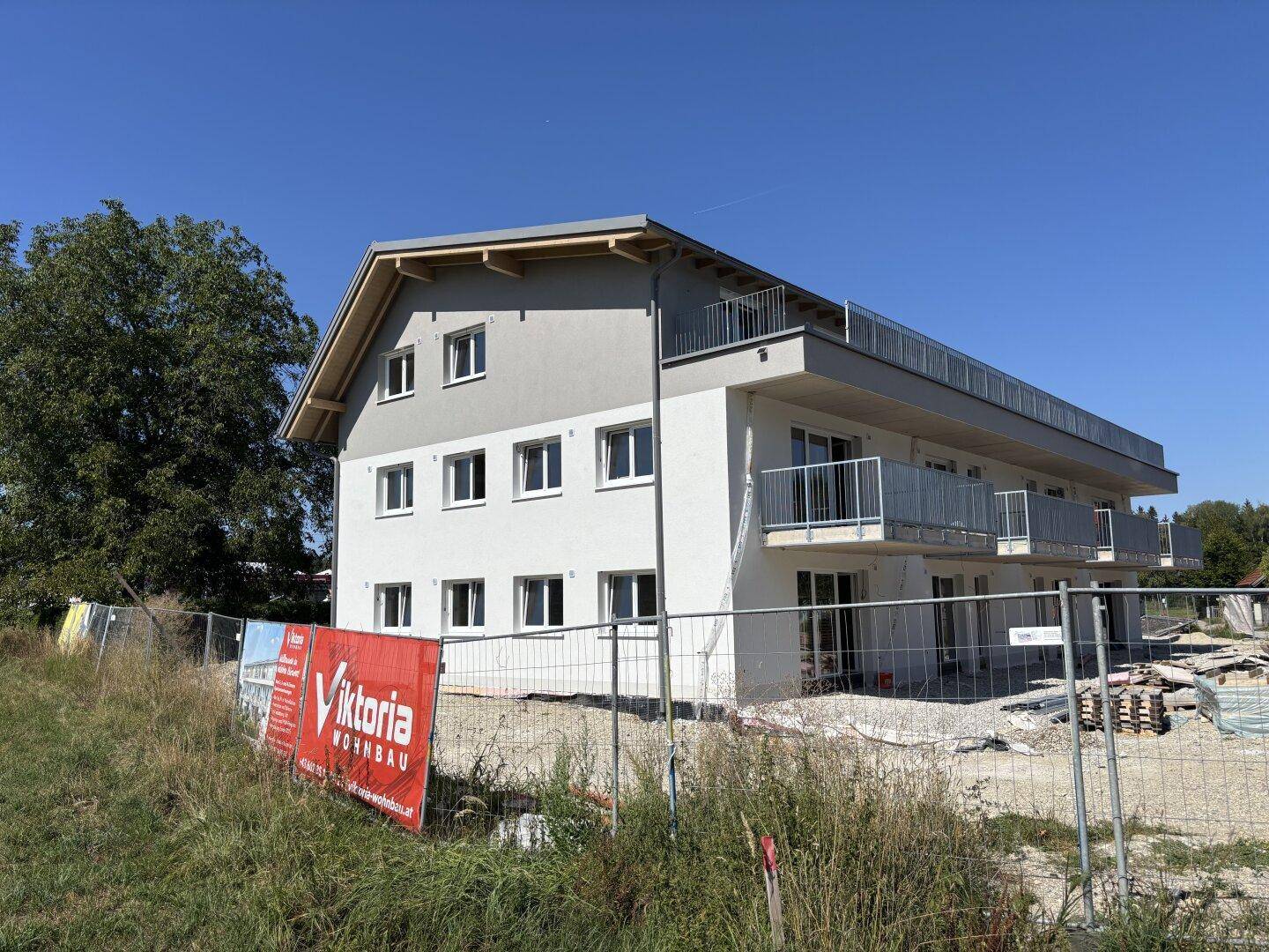 Neubau mit Werbebanner im Vordergrund und Balkonen unter strahlendem Himmel.