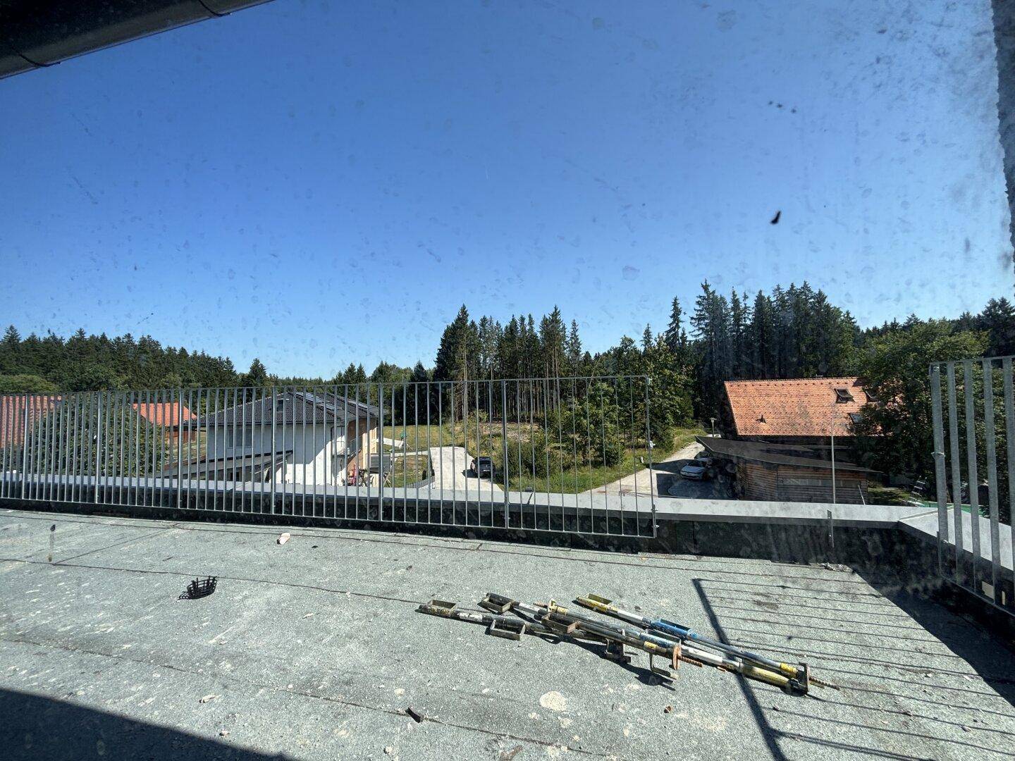 Unfertige Dachterrasse mit Metallgeländer und weitem Blick ins Grüne.