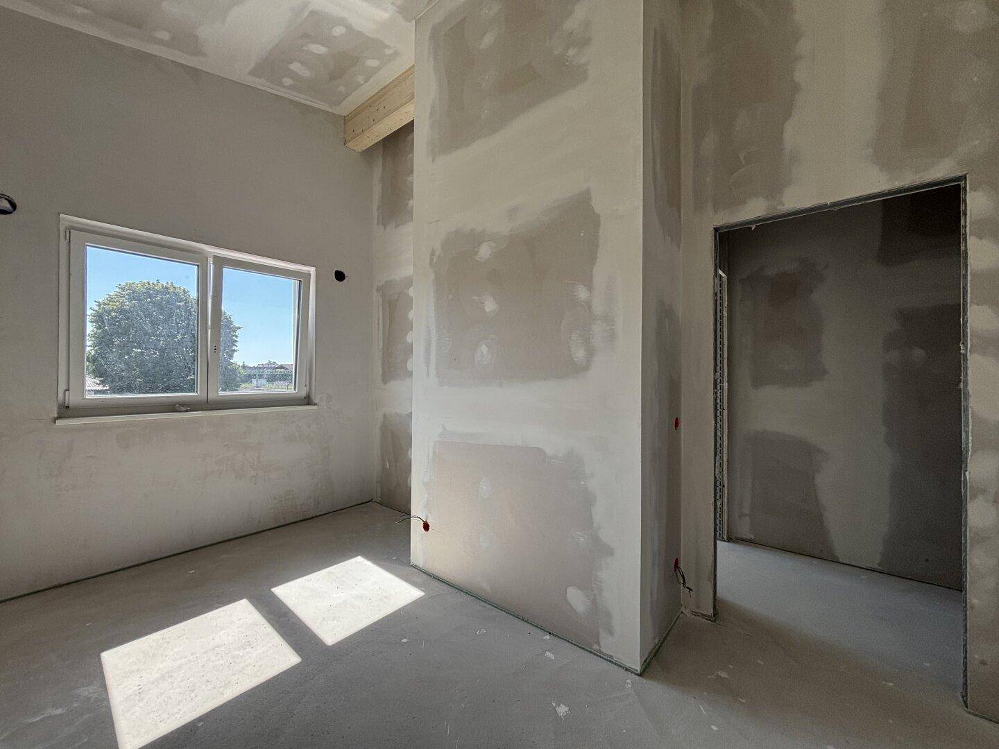 Heller, unfertiger Raum mit Fenster und Rohbauzustand, bereit für den Ausbau.