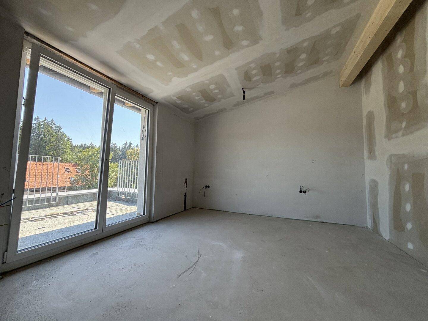 Unfertiges Zimmer mit schrägen Decken, großen Fenstern und Rohbauzustand.