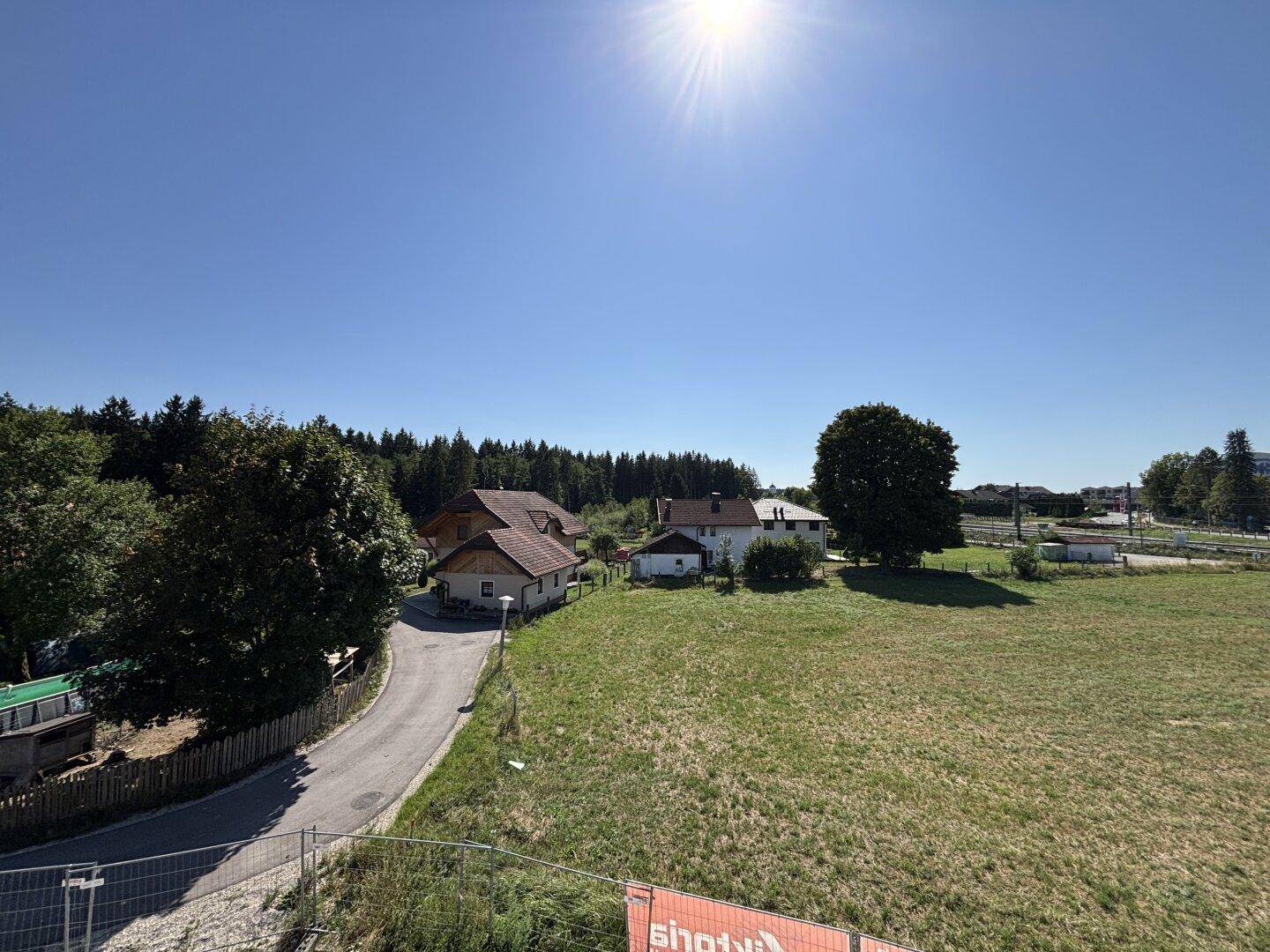 Weitläufiger Blick über grüne Felder und Wälder mit vereinzelten Häusern unter blauem Himmel.