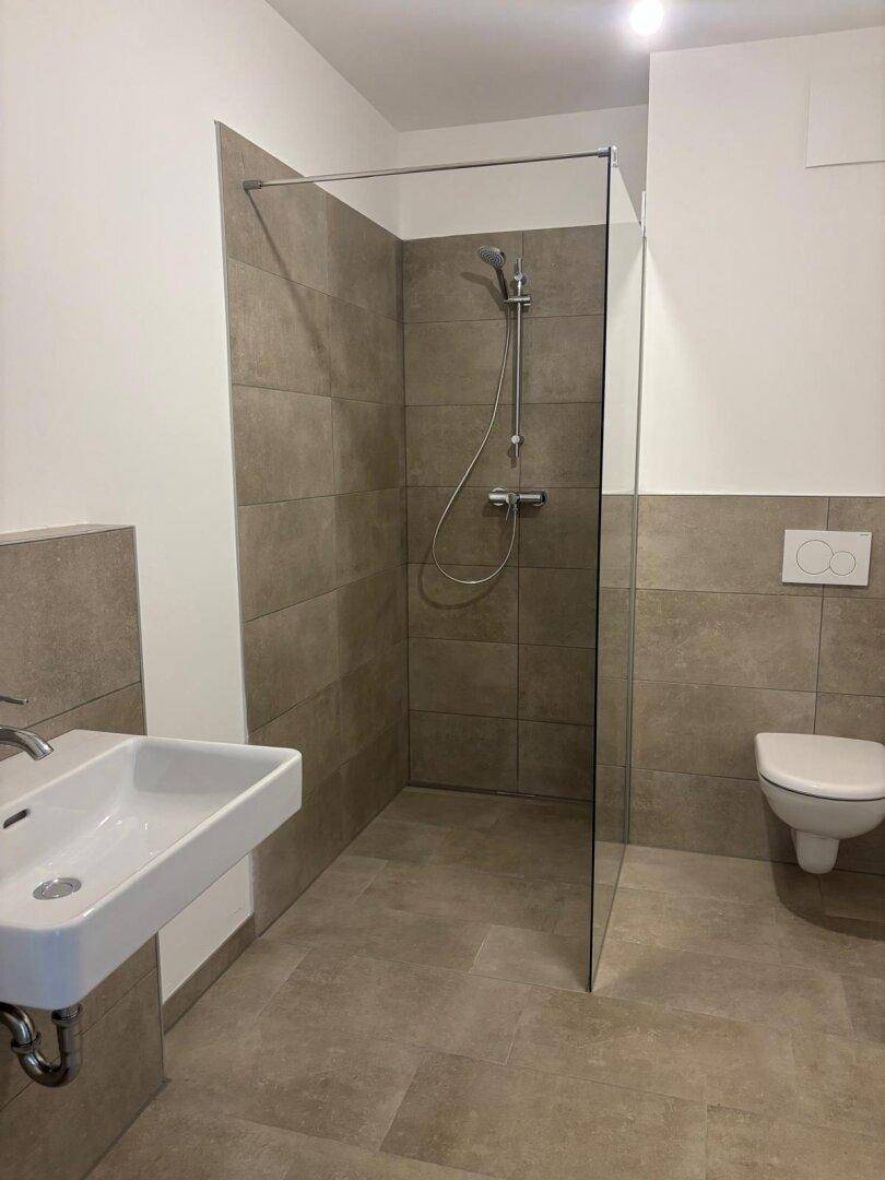 Modernes Badezimmer mit ebenerdiger Dusche, Wand-WC und Einzelwaschbecken in neuwertigem Zustand.