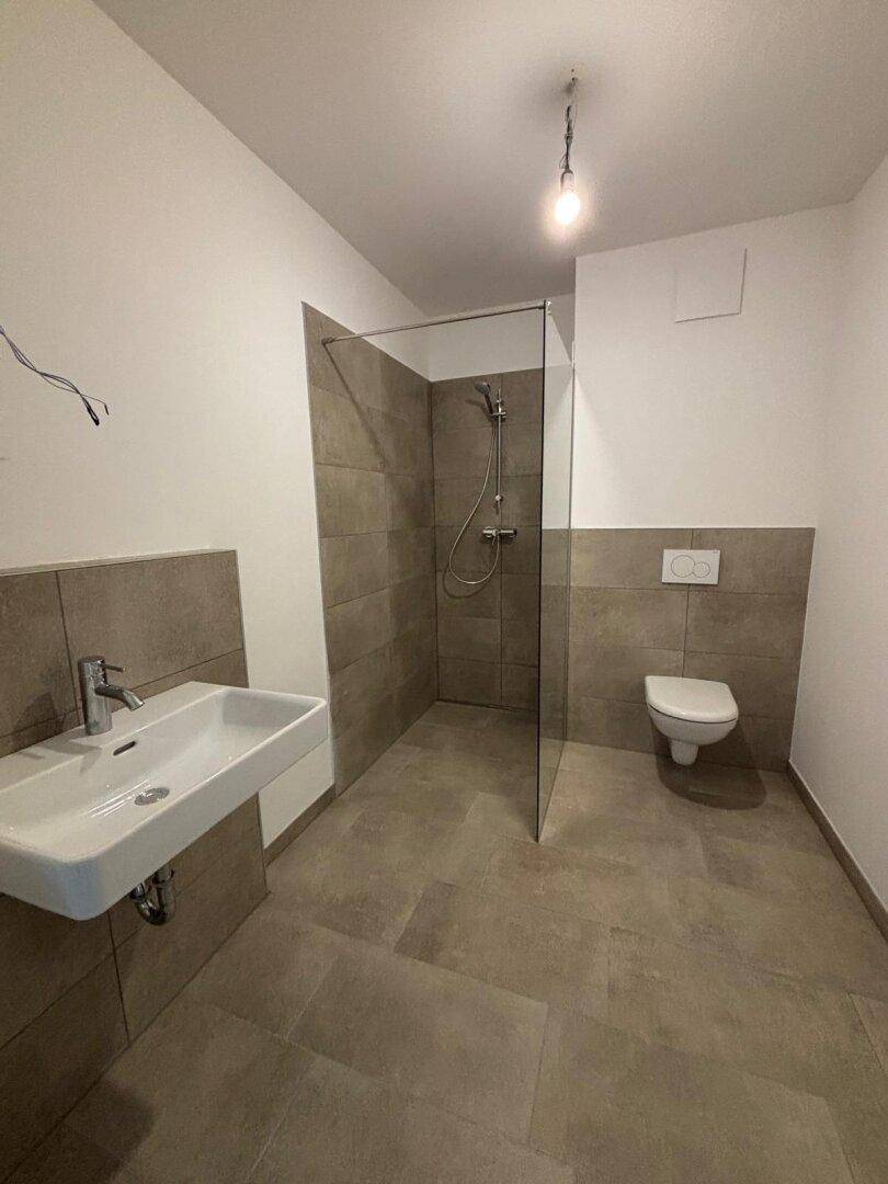 Geräumiges Badezimmer mit moderner ebenerdiger Dusche und hellen Fliesen.