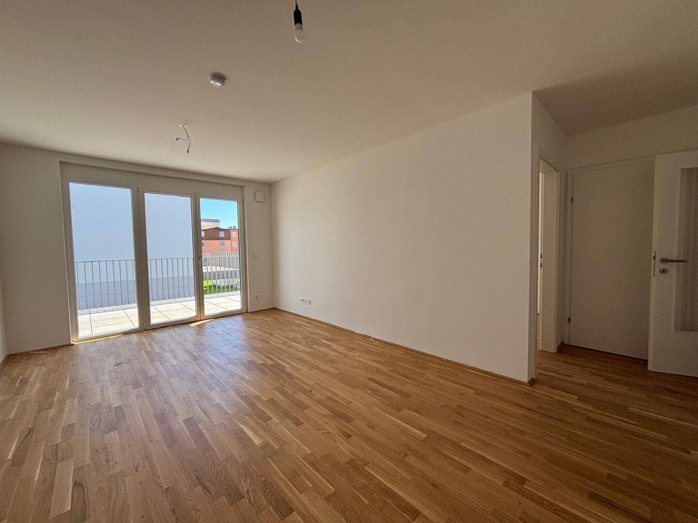 Helles Wohnzimmer mit Echtholzparkettboden und großen Fenstern mit Balkonzugang.