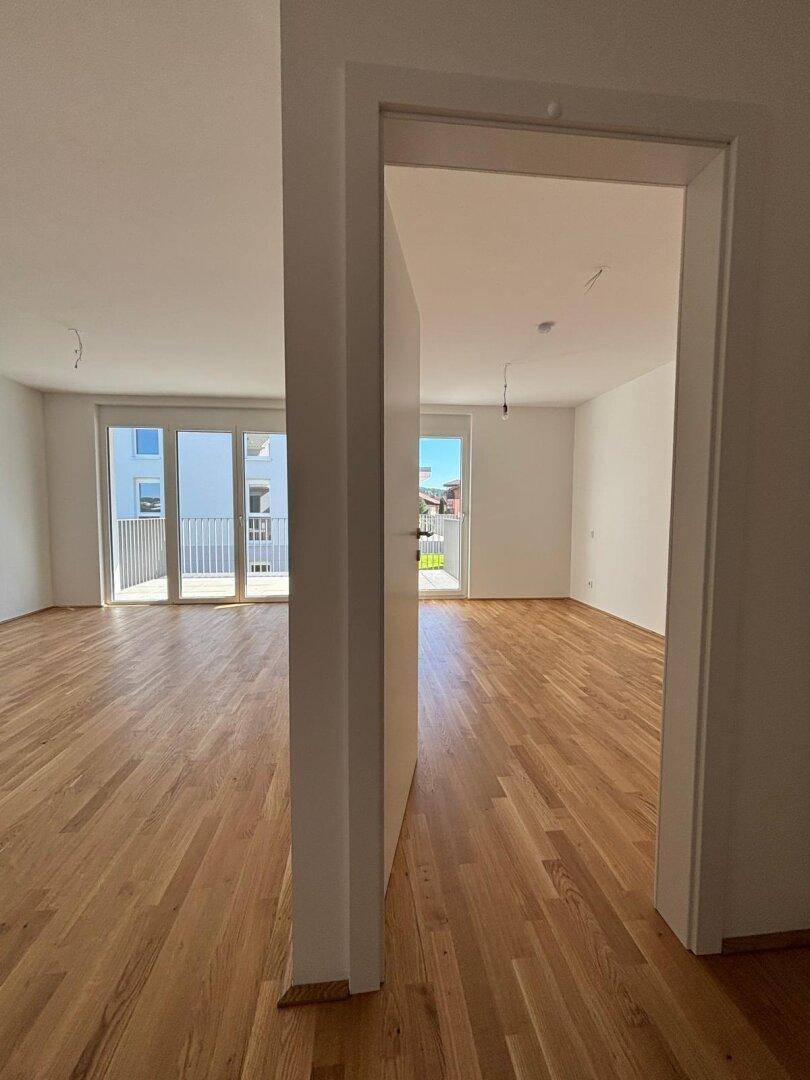 Lichtdurchflutetes Wohnzimmer mit Holzboden und Zugang zu einem sonnigen Balkon.
