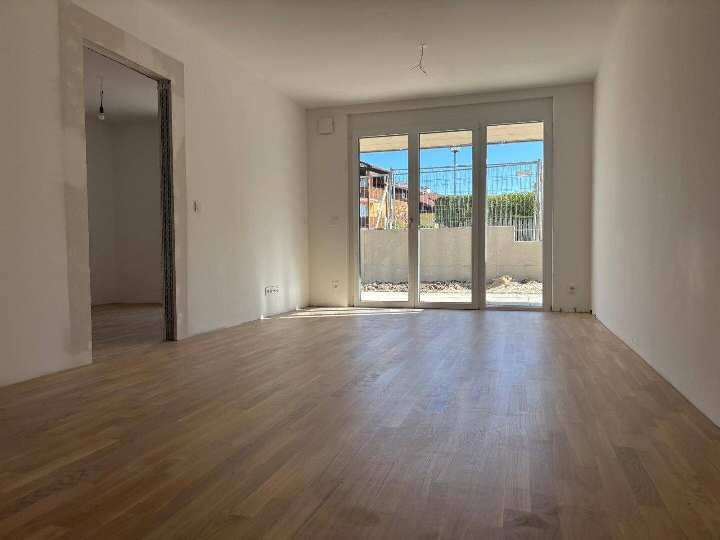 Lichtdurchflutetes Wohnzimmer mit Holzboden und großen Glastüren zum zukünftigen Außenbereich.