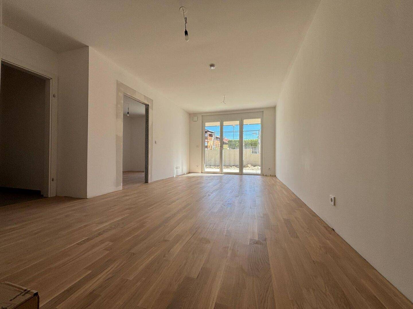 Helles, leeres Wohnzimmer mit neuem Parkettboden und großen Glastüren zum Außenbereich.