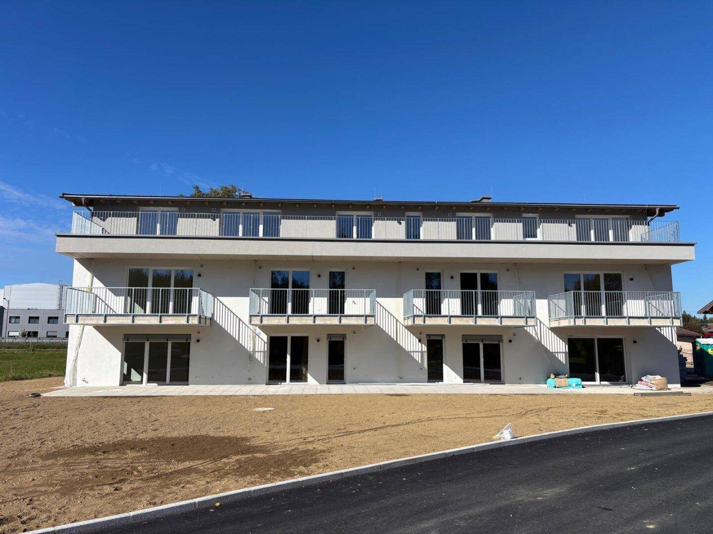 Vorderansicht des modernen Mehrfamilienhauses mit mehreren Balkonen und einer Dachterrasse.