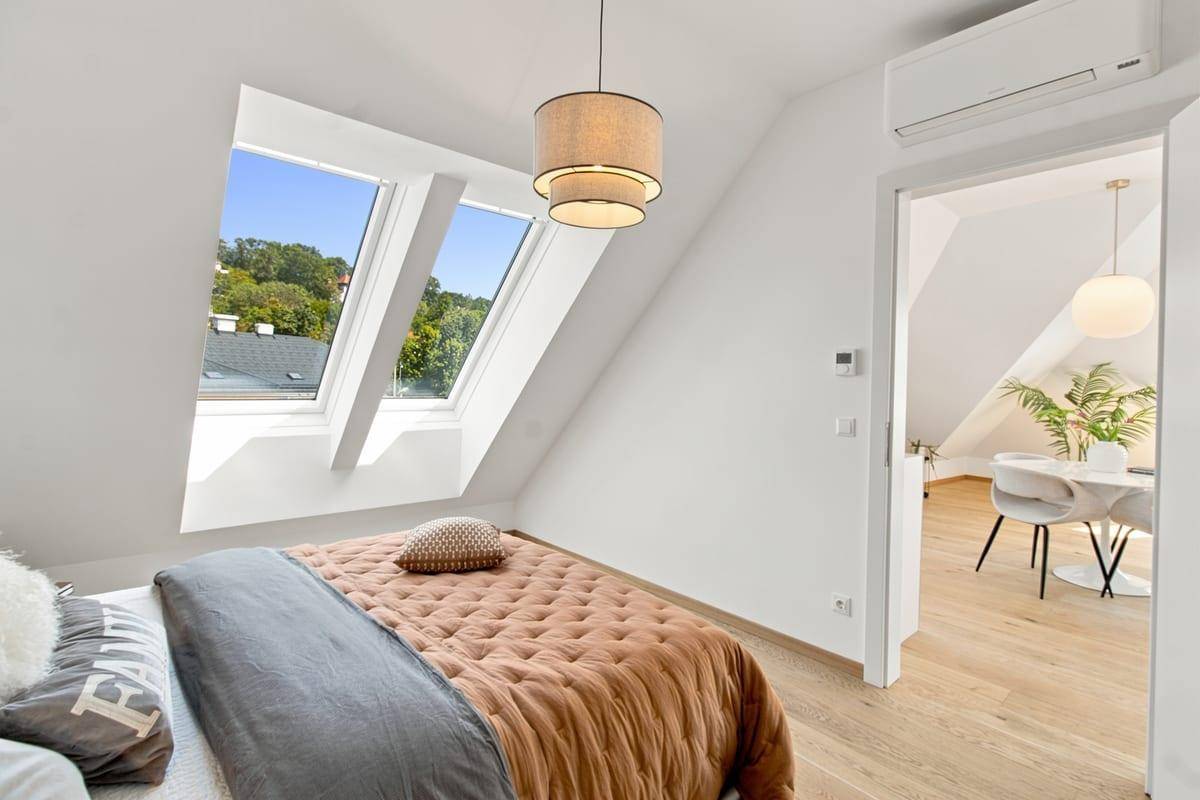 Helles Schlafzimmer mit Holzboden, Dachfenstern und Blick in den offenen Wohnbereich.