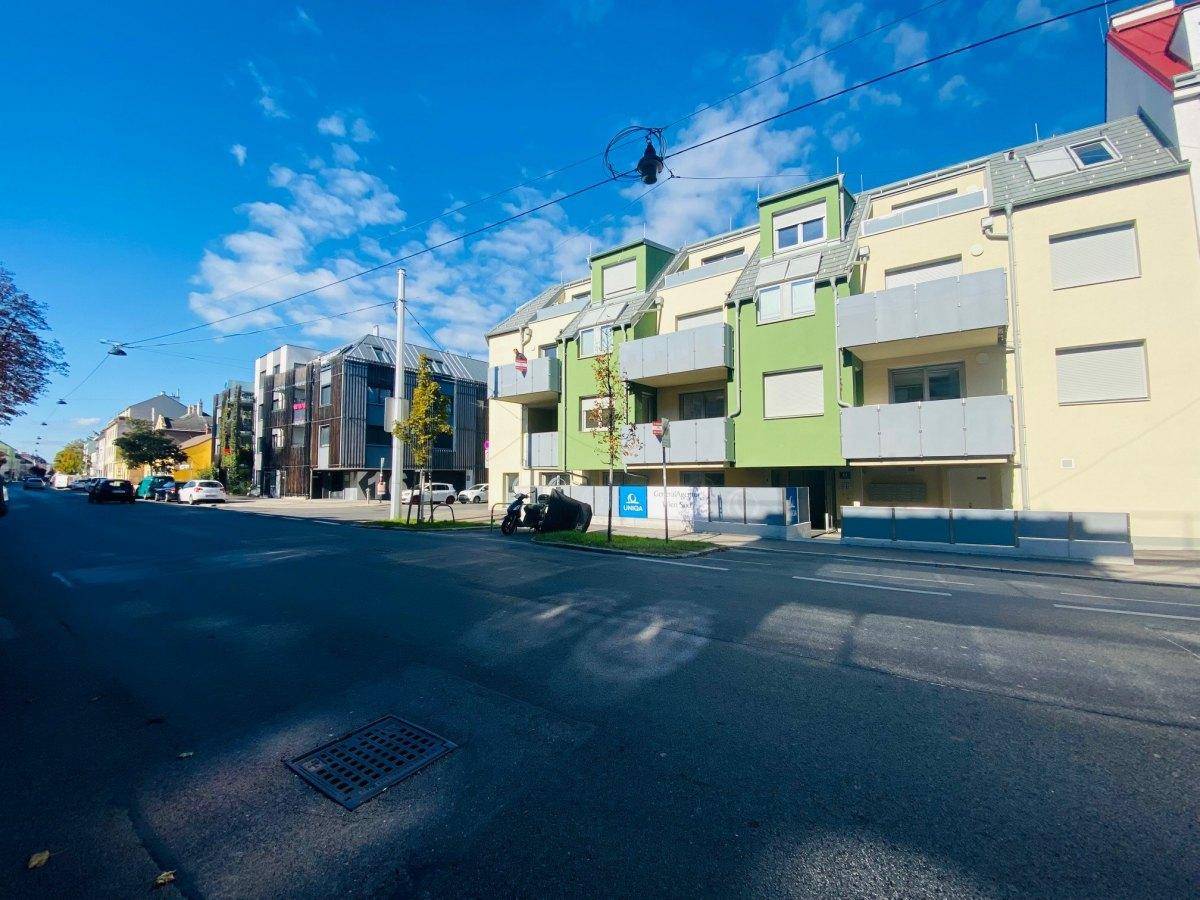 Ansicht des modernen Wohngebäudes mit grünen Akzenten und umliegender Stadtbebauung.