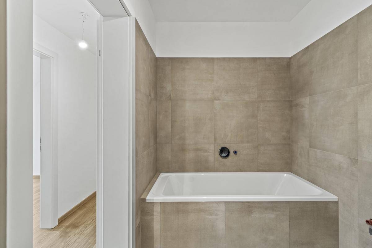 Modernes Badezimmer mit Badewanne und beigefarbenen Wandfliesen, die eine ruhige Atmosphäre schaffen.