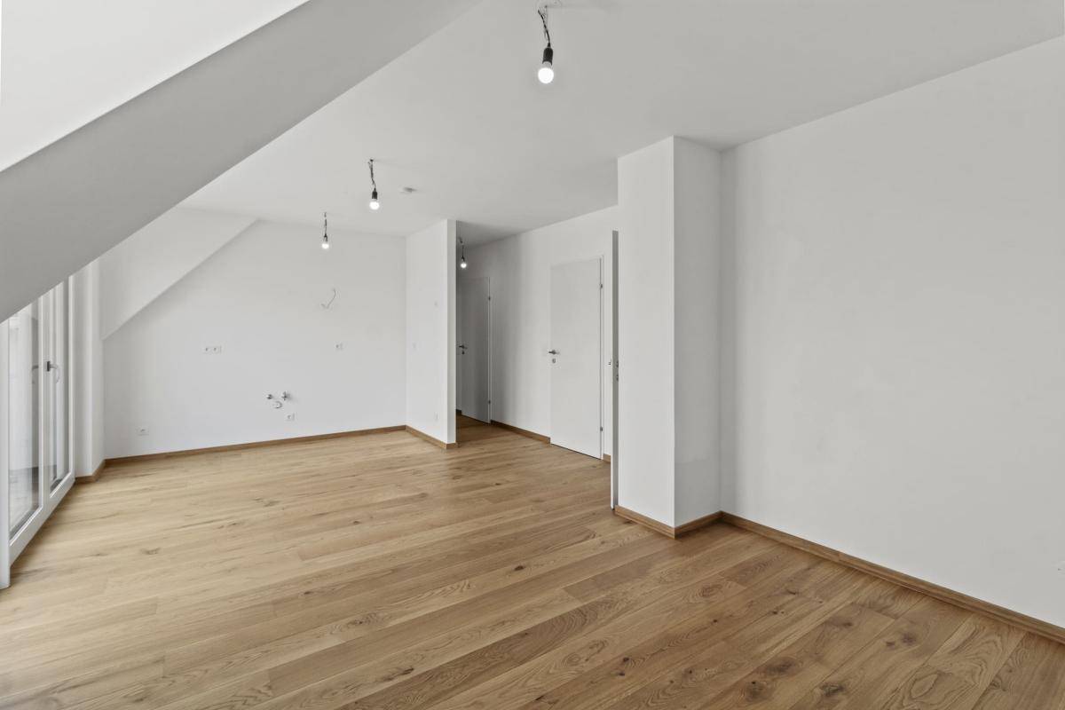 Geräumiger Wohnbereich mit Holzboden, weißen Wänden und Dachschräge, bereit für die Einrichtung.