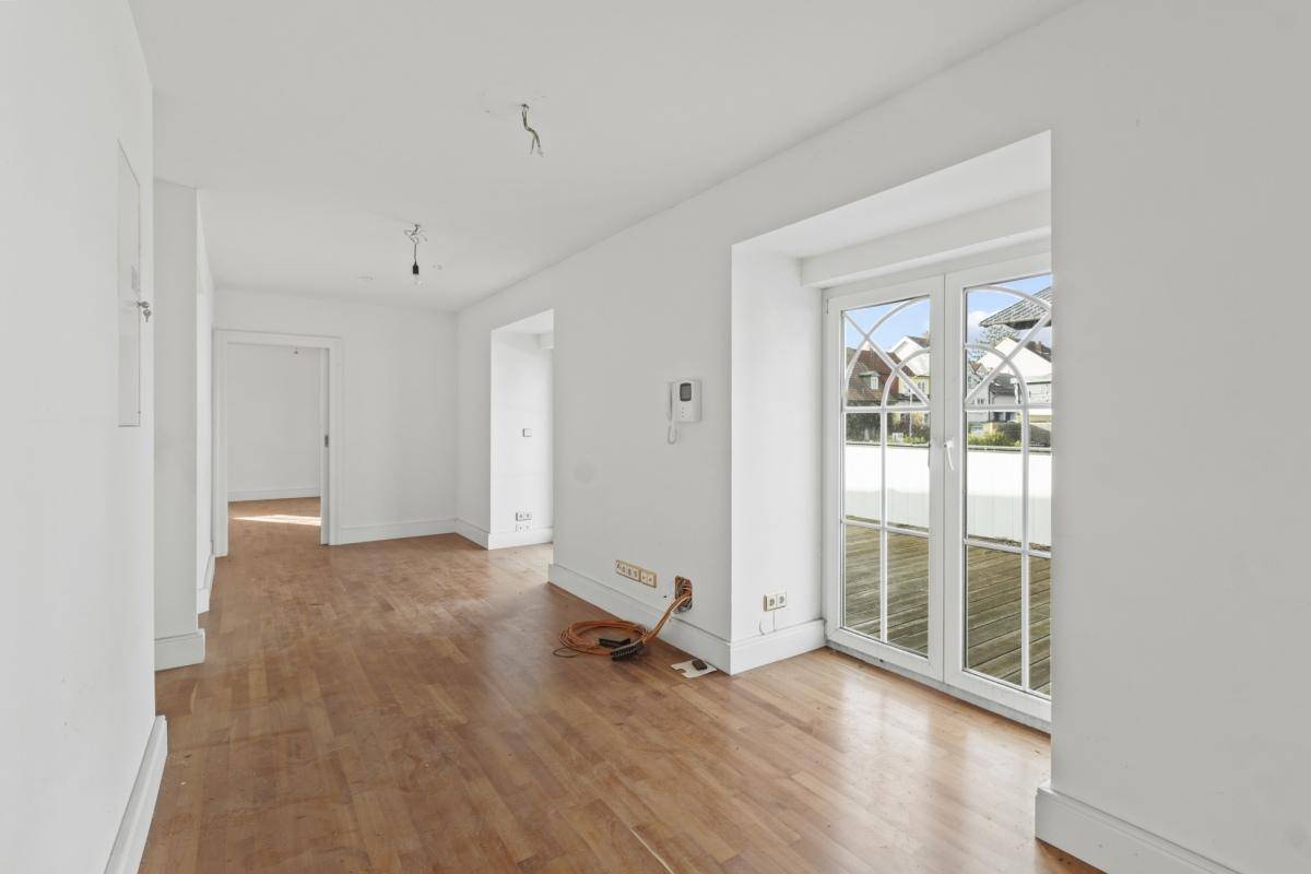 Heller Raum mit Holzboden und großen Fenstern, die viel Tageslicht hereinlassen.